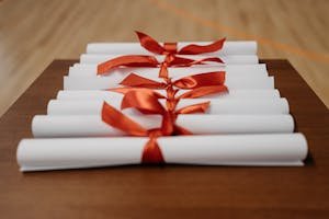 Close-up of rolled diplomas tied with red ribbons on a wooden desk, ready for presentation.